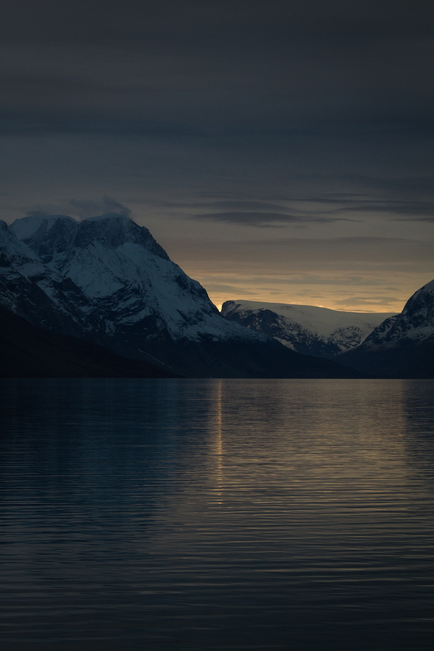 The final moments of sunset diffract up and through the narrow conjunction of two Arctic mountains, reflecting as a thin line across King Oscar Fjord, and peace descends over the landscape.