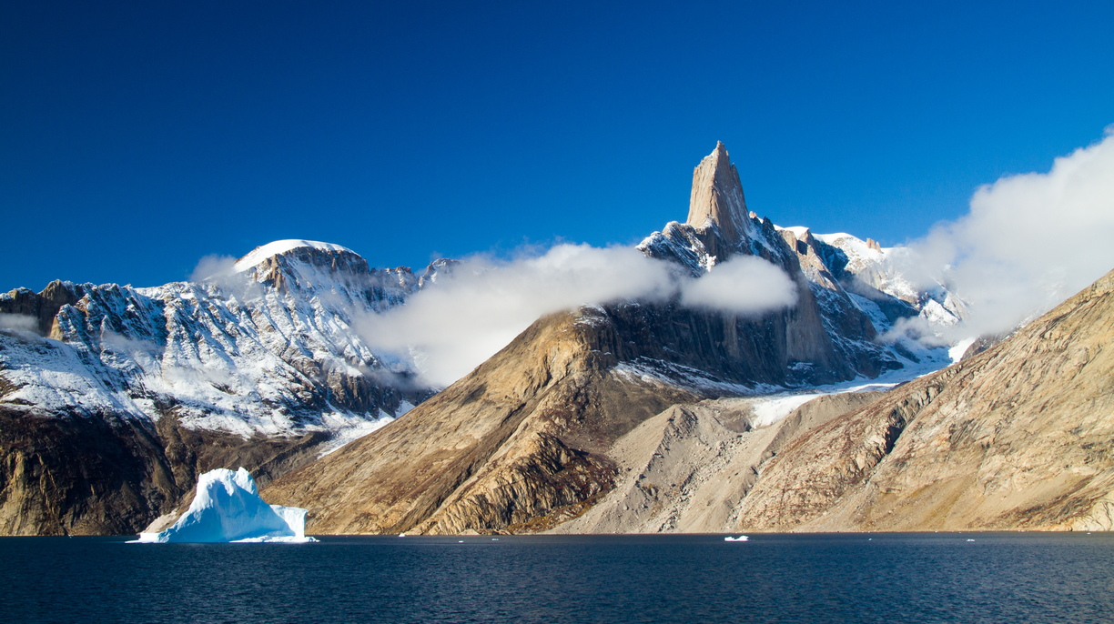 Exploring Greenland’s fjord systems, I stumbled upon this wild and immense landscape which immediately stole my heart. The singular pinnacle of rock nestled among blue skies, was framed by blankets of cloud, and dwarfed passing icebergs which paraded past. It was like nothing I’d ever seen before.Notes: From the deck of a ship