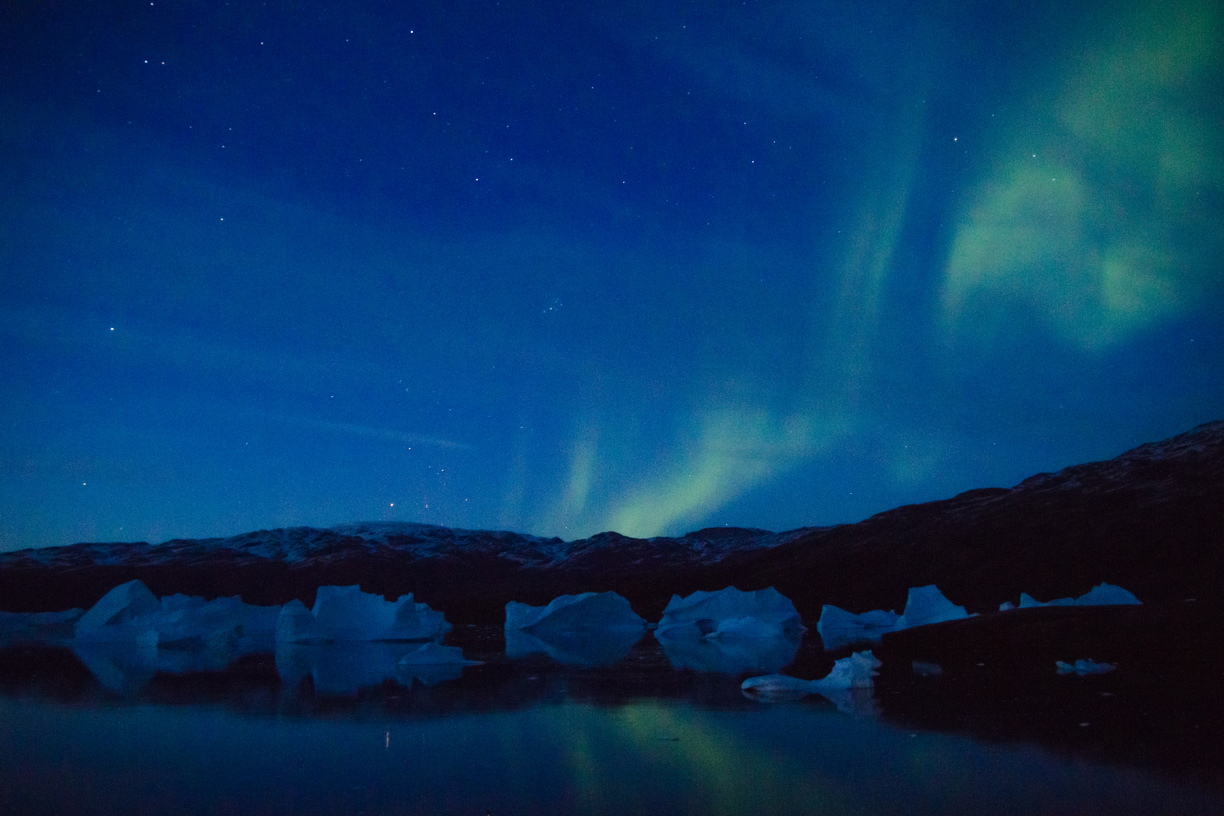 Curtains of green aurora borealis twist over the icebergs and mountains of Rypefjord, Greenland